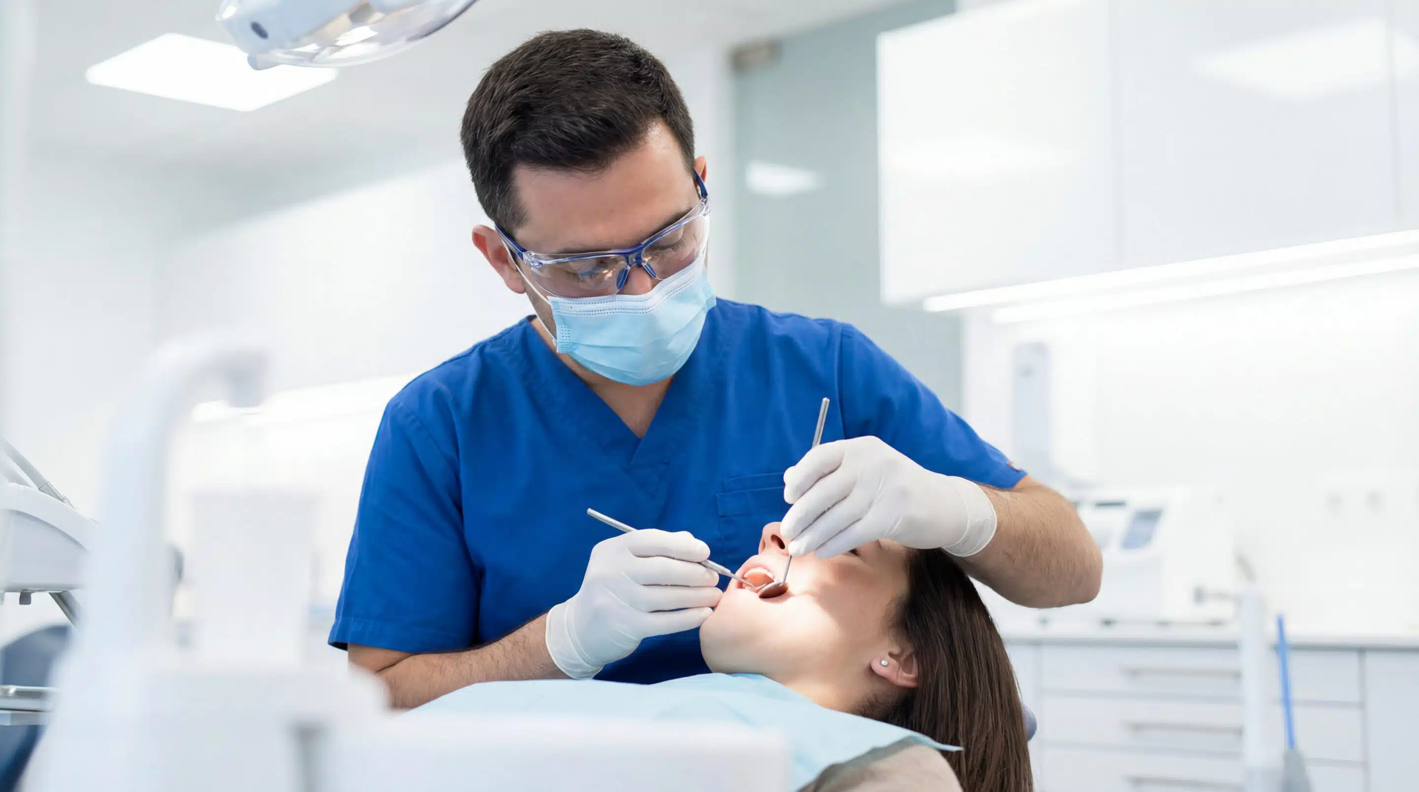 Dentist examining female patient in bright clinic chair with mir